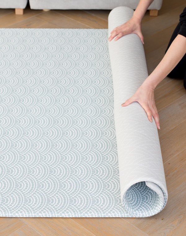 Unrolling a double sided memory foam baby floor mat that is designed for modern family spaces including a scalloped motif and on the reverse a geometric chevron