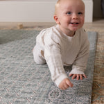 Baby crawling on a cushioned play mat with a Persian rug design