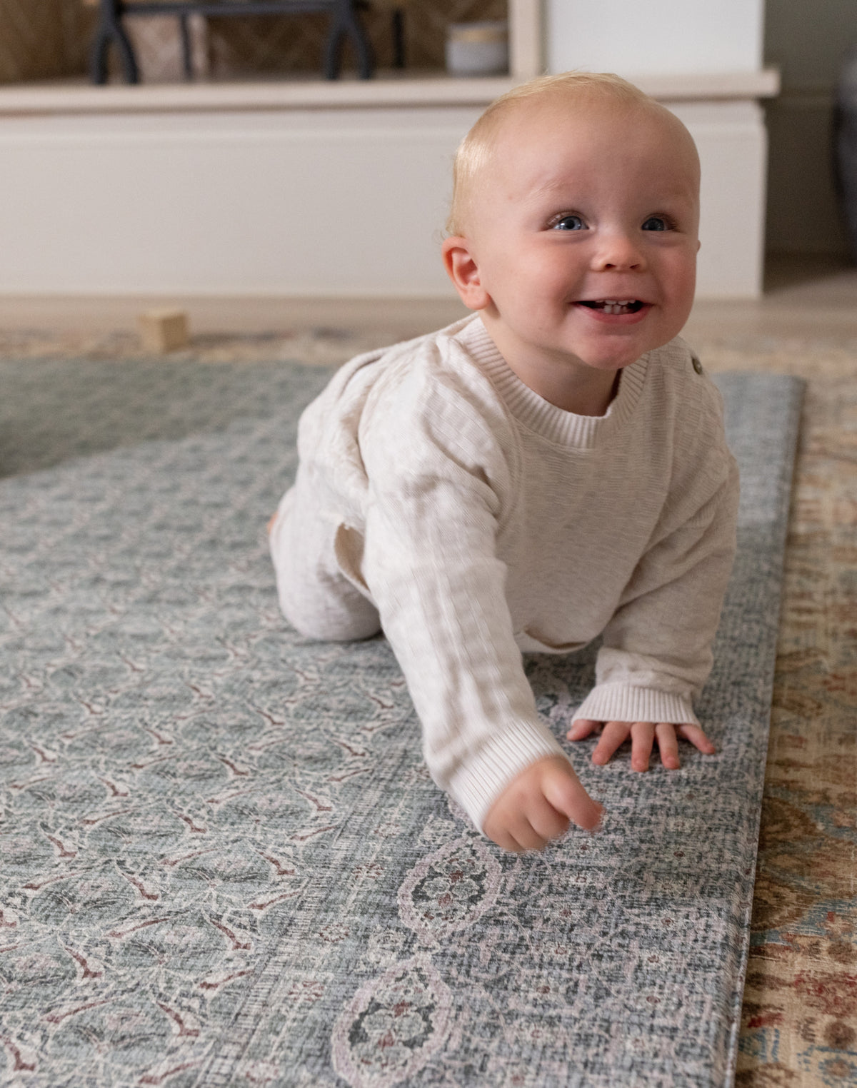 Baby crawling on a cushioned play mat with a Persian rug design