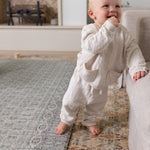 Standing toddler smiling on soft sage baby mat in living room