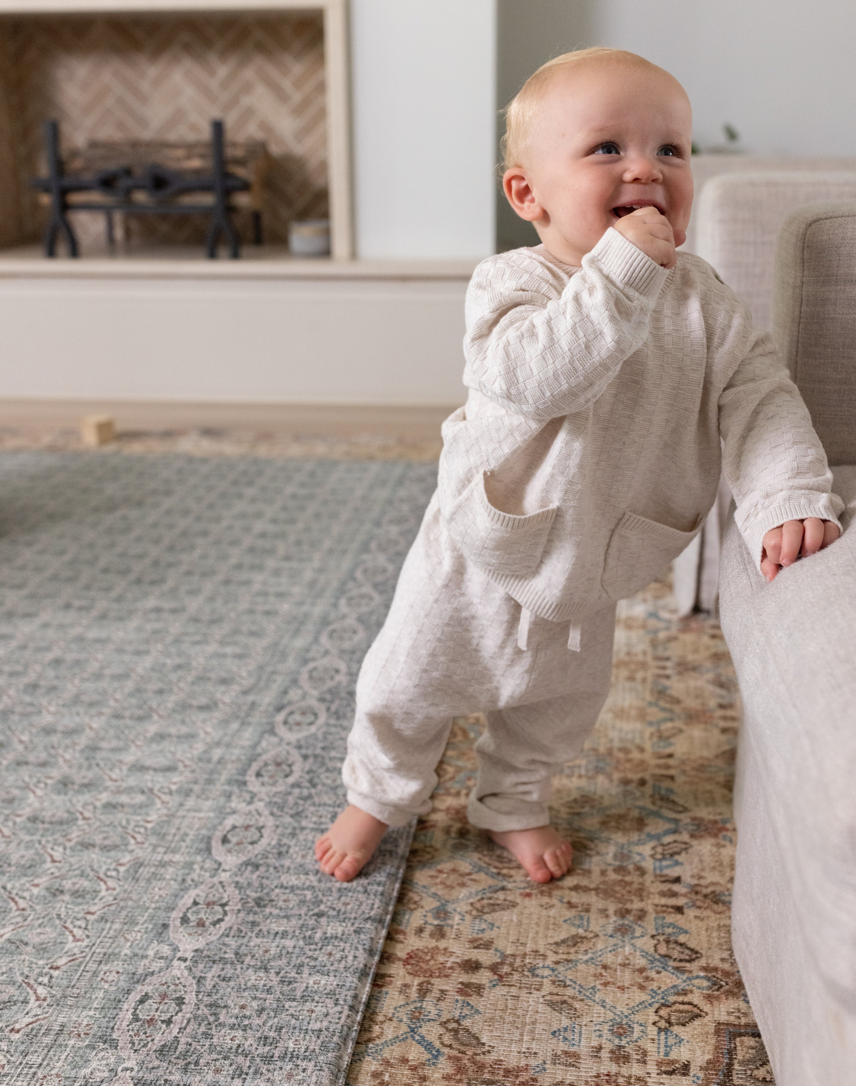Standing toddler smiling on soft sage baby mat in living room