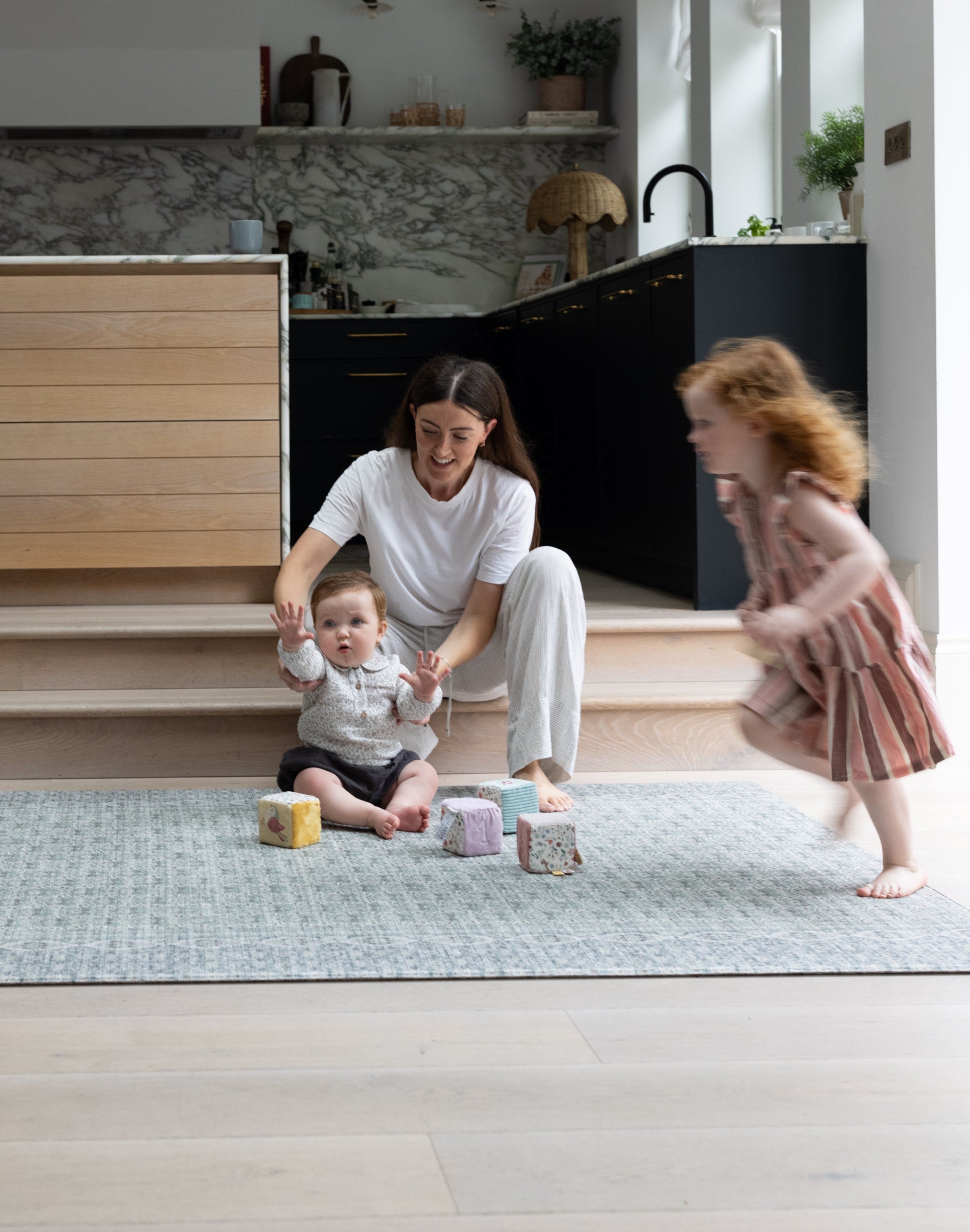 Mum and two children playing  with toys on a thick playmat rug in a modern home