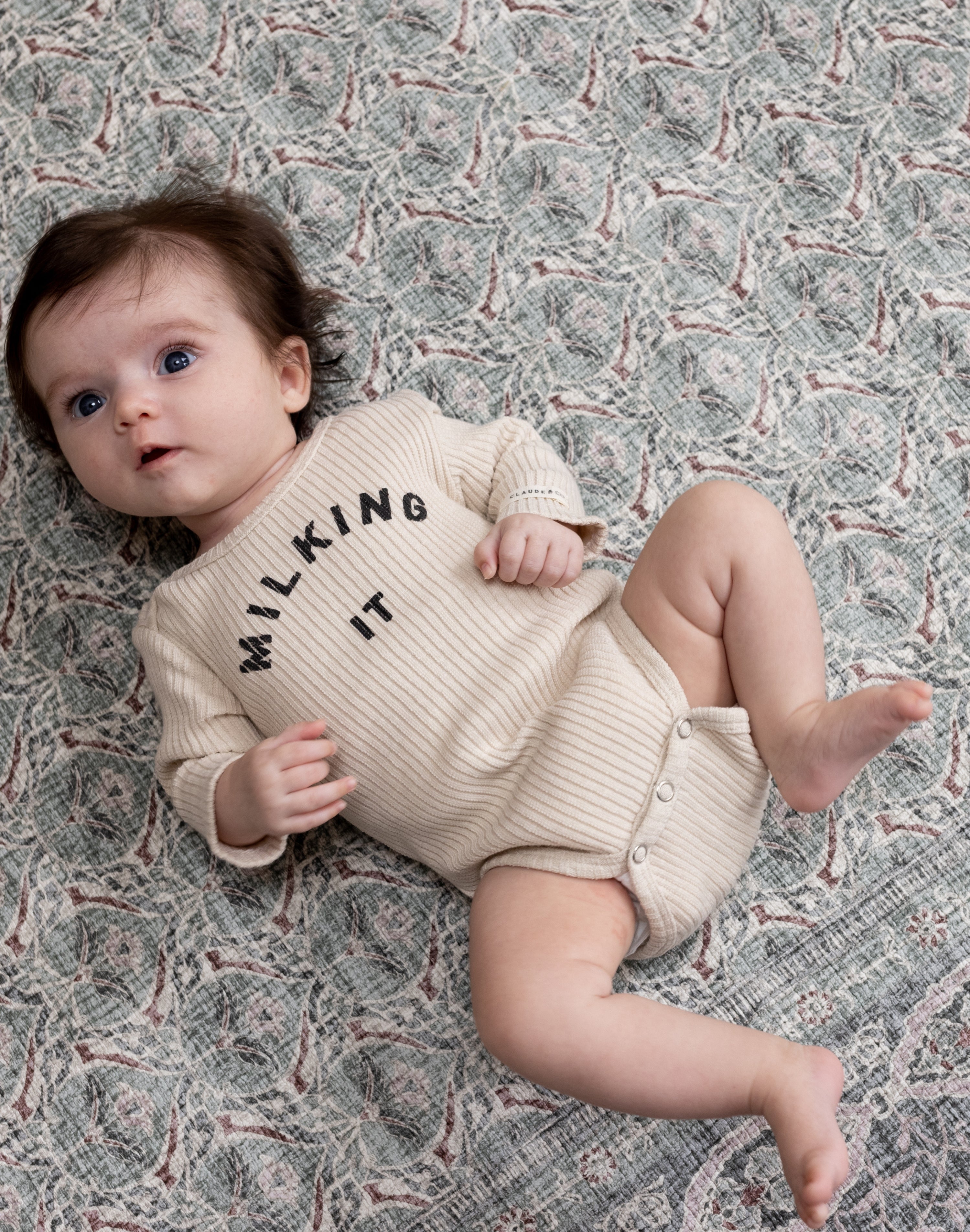 Baby lying happily on patterned green Totter + Tumble baby rug play mat