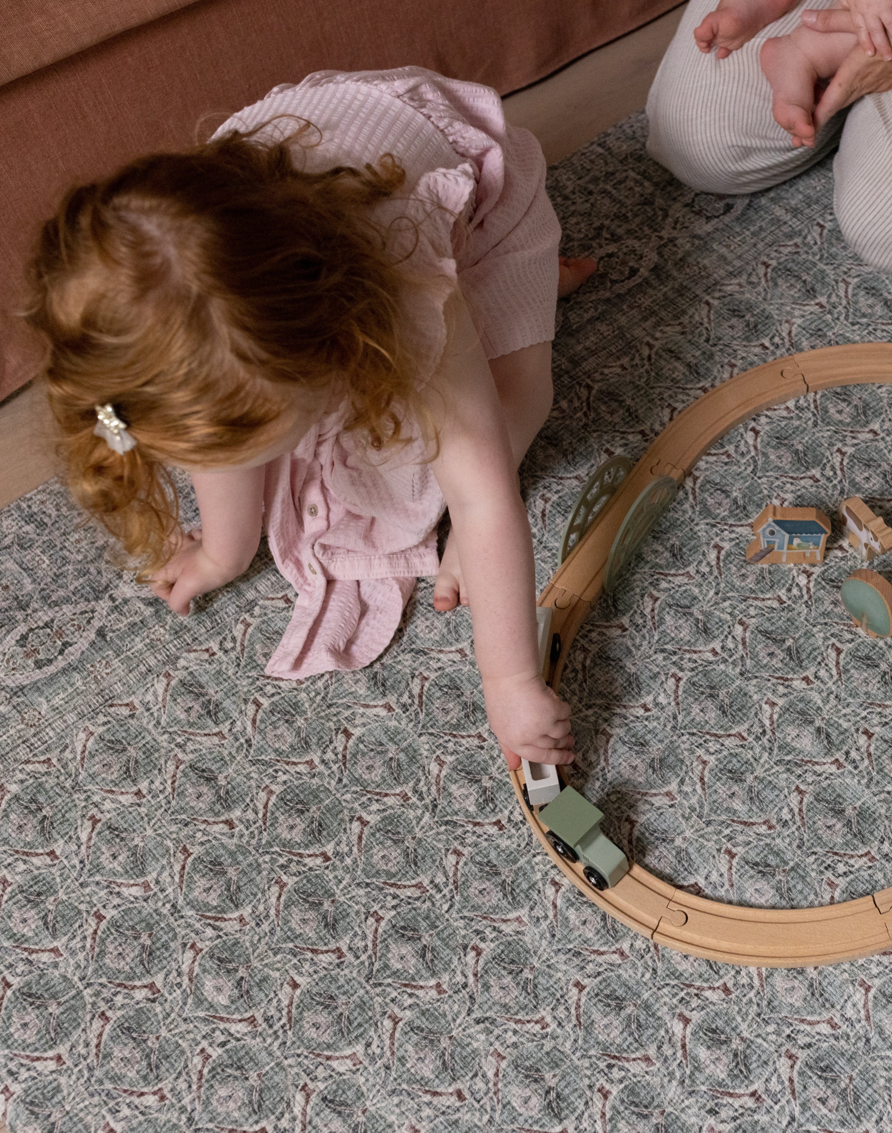 Overhead of a child playing with a toy train set on a patterned baby mat