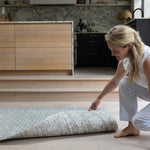 Woman unrolling a double sided playmat on a wooden floor in a modern kitchen.