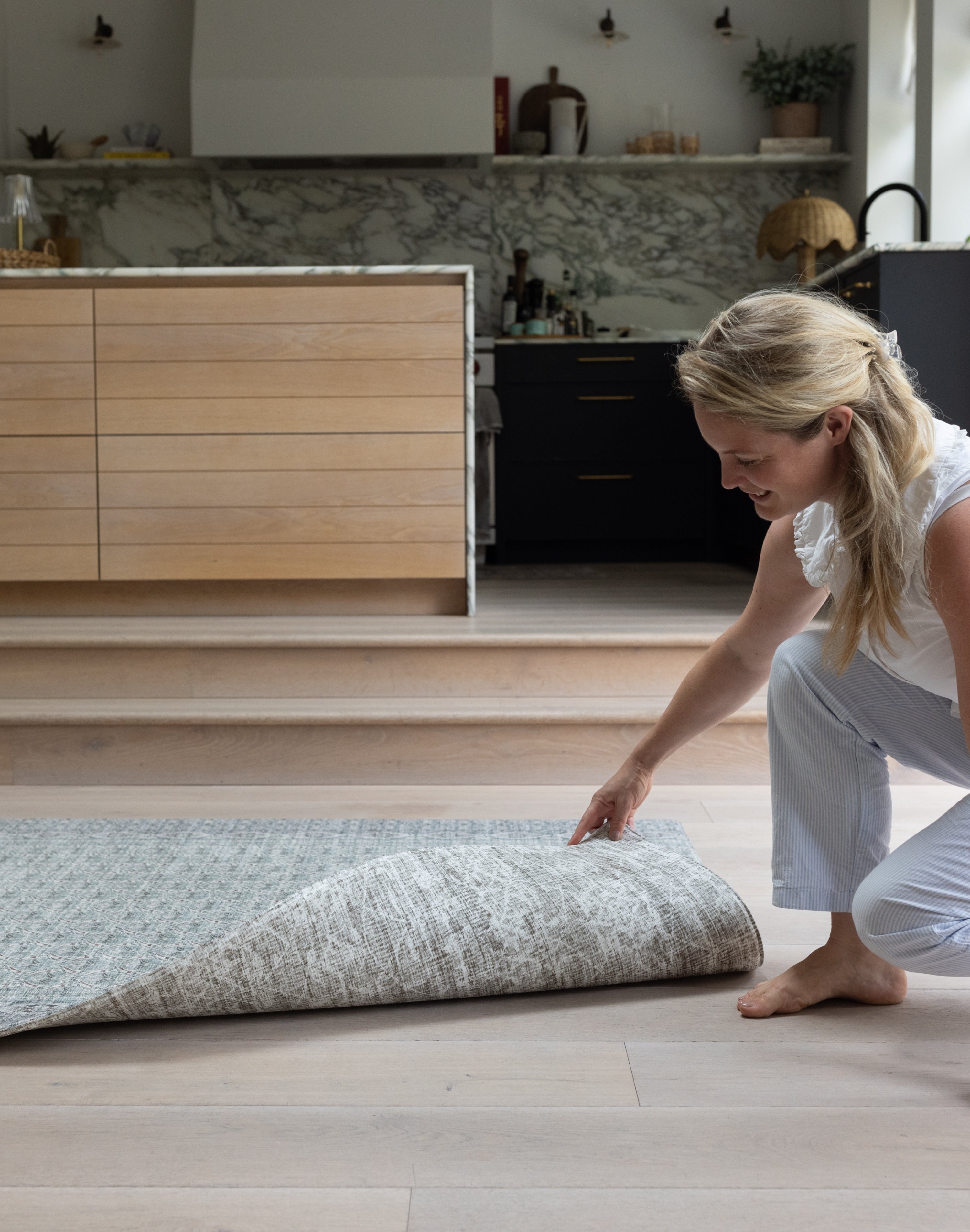 Woman unrolling a double sided playmat on a wooden floor in a modern kitchen.