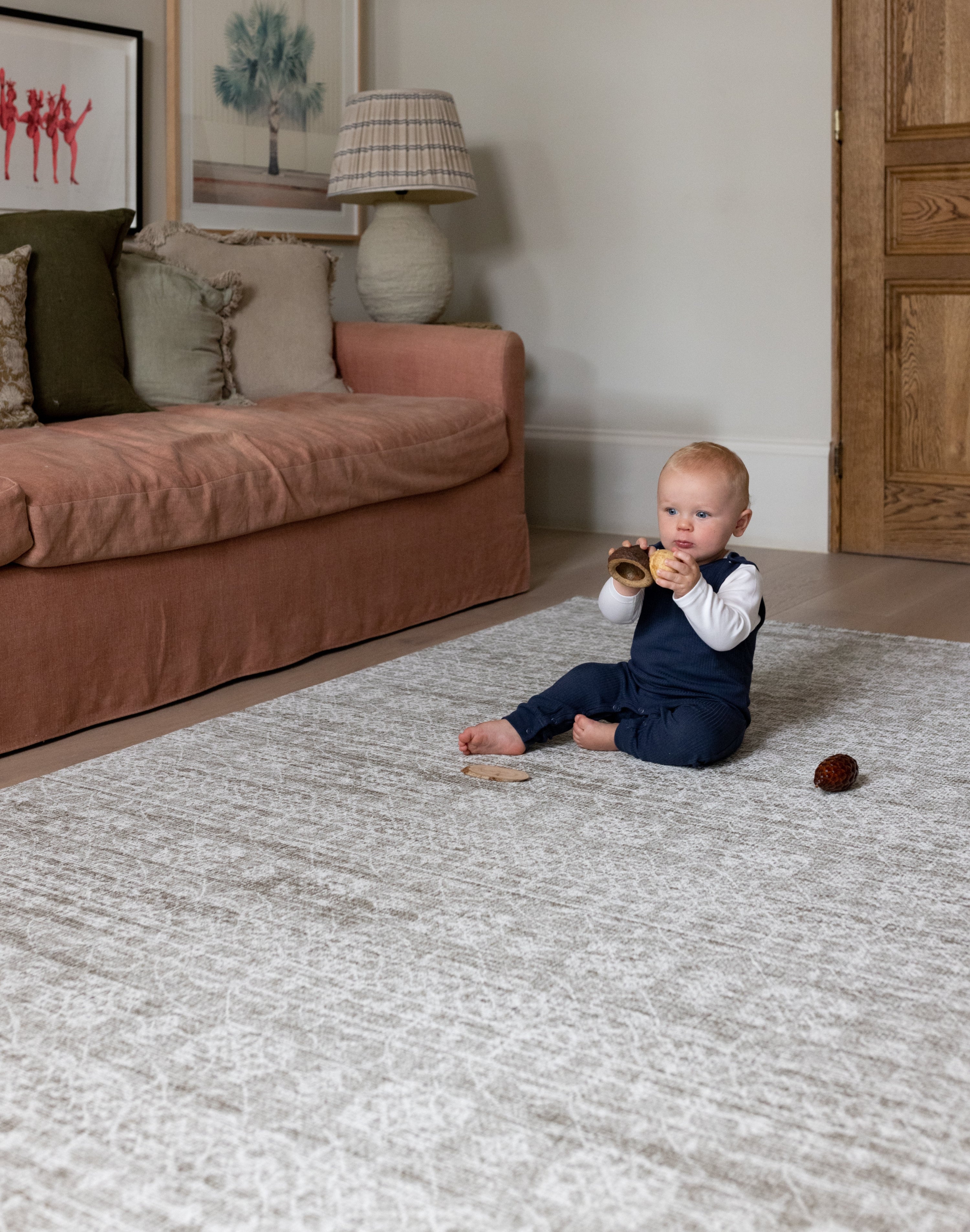 A baby plays on a textured play mat in a dusty pink  family room
