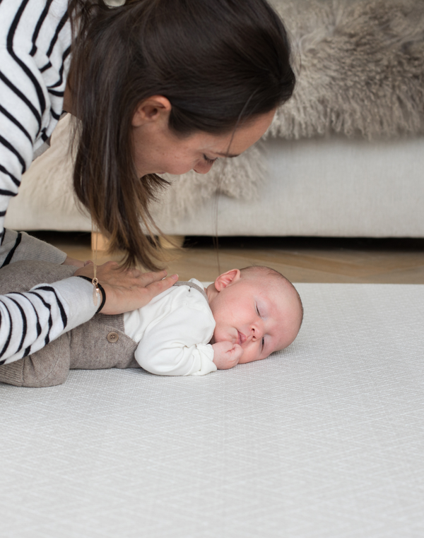 Lady strokes baby as they sleep on their front on a memory foam playmat that is comfortable for all floor time activities