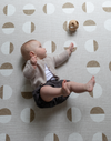 Little baby rolls during floor play with a cushy tan play mat as the ideal play base