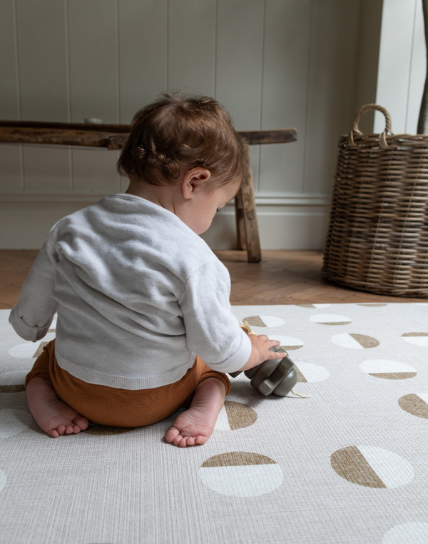 Baby is supported on baby play rug with a neutral organic motif that is beautiful in family homes
