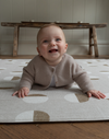 Baby lays on foam tan floor mat with non toxic materials that are safe from birth