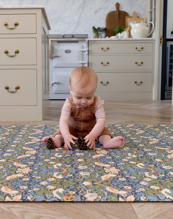 Baby sitting on iconic Strawberry Thief design play mat with thick memory foam to support and protect on hard wood flooring playing with pine cones