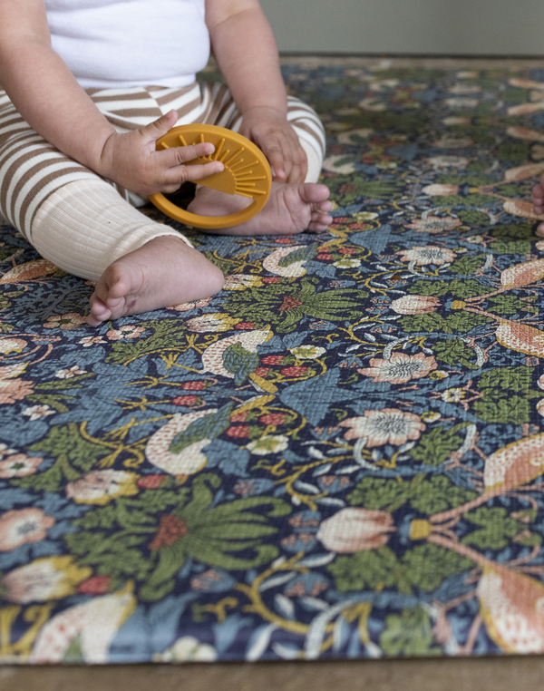 Baby sitting and playing on thick memory foam play mat by Totter and Tumble with Strawberry Thief design from William Morris archive supportive and protective for babies development