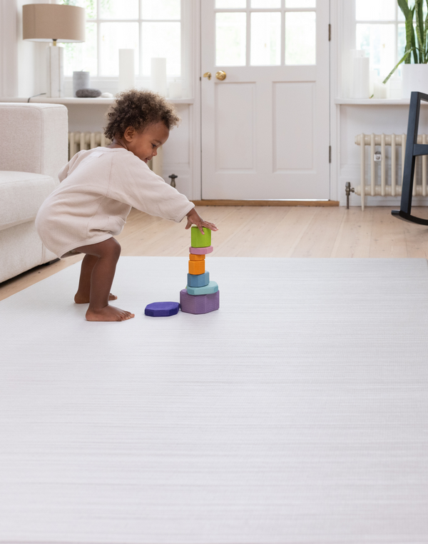 Toddler stacking wooden toys on the Tumble mats in tan and beige ombre design for support during floor play