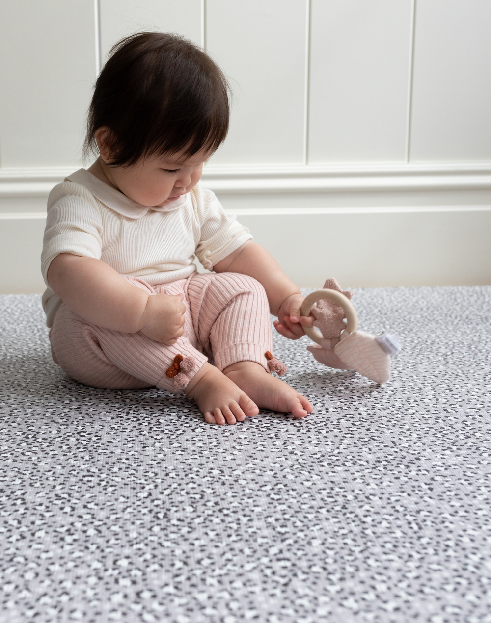 Baby girl playing with baby toy on non toxic kids play mat with grey leopard print pattern