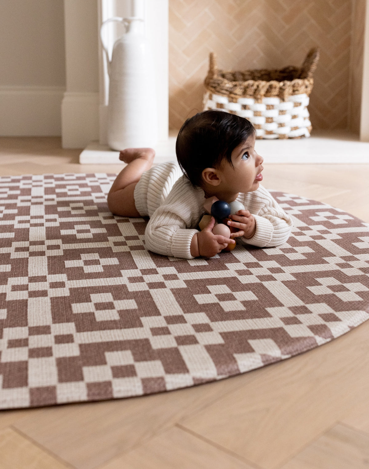 A baby crawls on a round brown patterned play mat. The room has stylish neutral tones