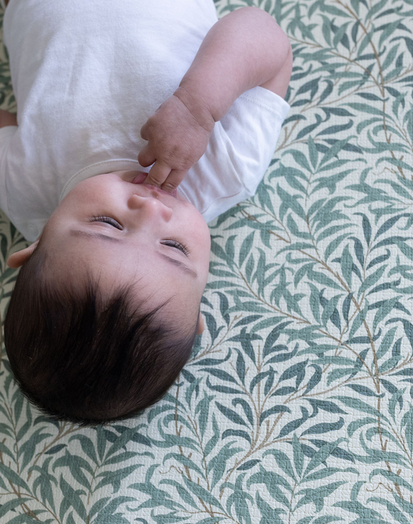 Baby laying relaxed on Willow Boughs play mat by Totter and Tumble in collaboration with heritage design group Morris & Co. keeping babies comfy for floor play and supporting developmental milestones