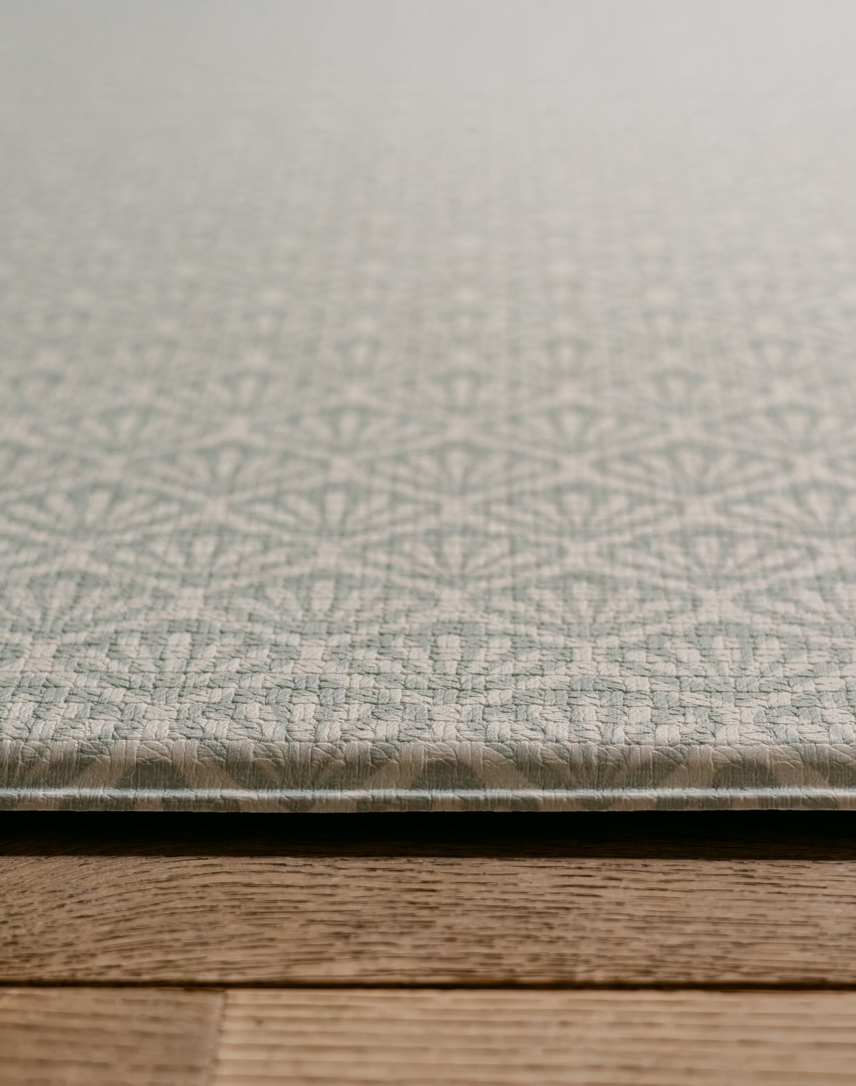 A close-up of the Beachcomber play mat  with a repeating geometric shell pattern, resting on a wooden surface. | SKU: 26 BEACH/GATHER XL, 26 BEACH/GATHER STD, 26 BEACH/GATHER COMP
