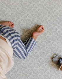 A baby crawling safely and comfortably on the beachcomber shell design play mat from totter and tumble