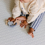 A baby sat comfortably on The Beachcomber play mat. With a repeating shell design. | SKU: 26 BEACH/GATHER XL, 26 BEACH/GATHER STD, 26 BEACH/GATHER COMP