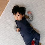 A baby laying comfortably on thick memory foam, coastal inspired rug-like design play mat from totter and tumble | SKU: 26 BEACH/GATHER XL, 26 BEACH/GATHER STD, 26 BEACH/GATHER COMP