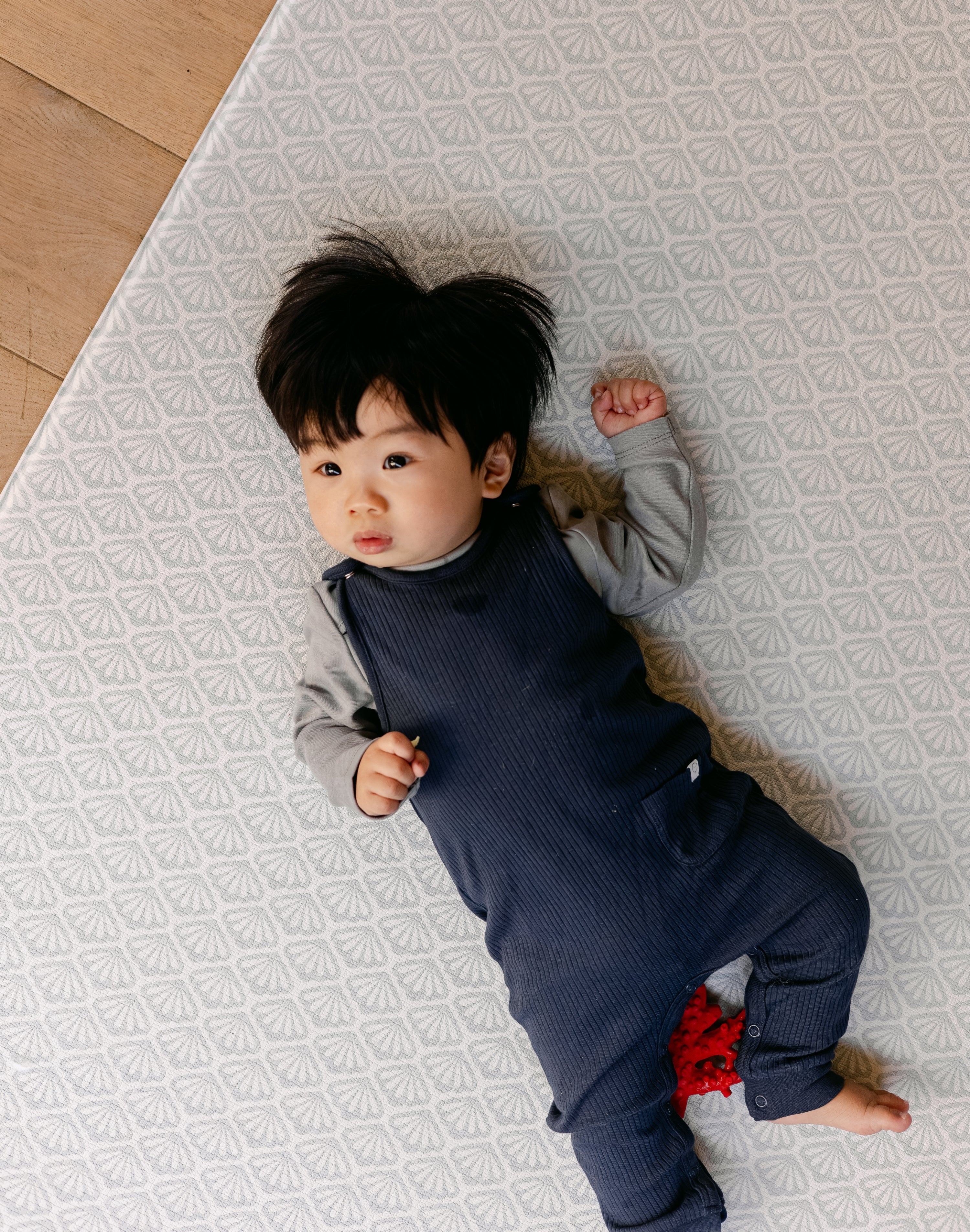 A baby laying comfortably on thick memory foam, coastal inspired rug-like design play mat from totter and tumble | SKU: 26 BEACH/GATHER XL, 26 BEACH/GATHER STD, 26 BEACH/GATHER COMP