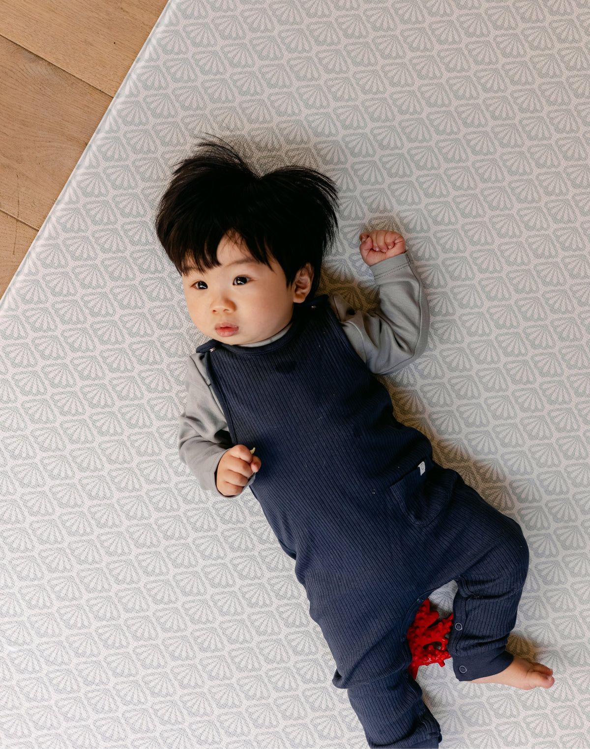 A baby laying comfortably on thick memory foam, coastal inspired rug-like design play mat from totter and tumble | SKU: 26 BEACH/GATHER XL, 26 BEACH/GATHER STD, 26 BEACH/GATHER COMP
