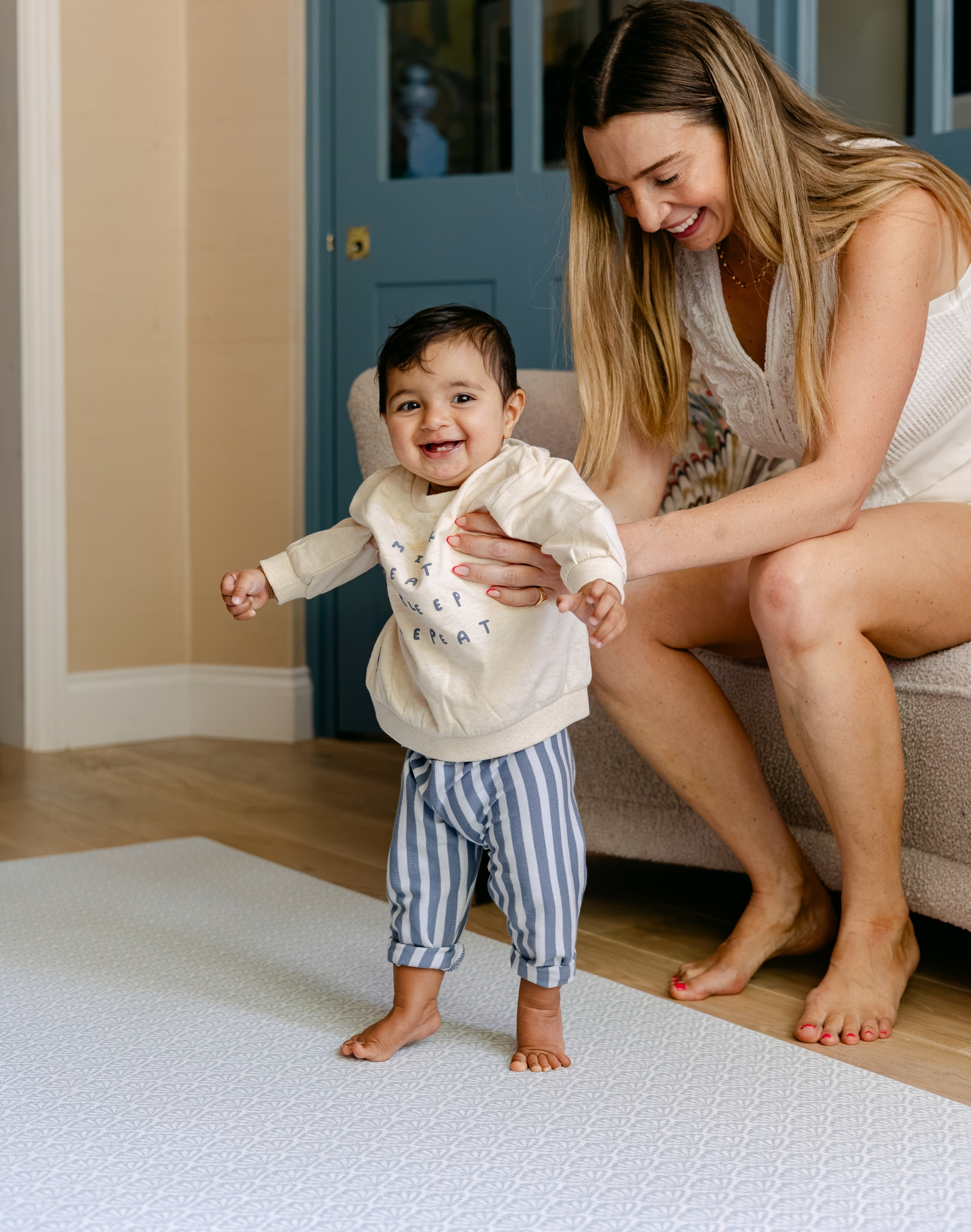 A woman helping a baby stand up safely on The Beachcomber play mat, made from thick safe non toxic memory foam | SKU: 26 BEACH/GATHER XL, 26 BEACH/GATHER STD, 26 BEACH/GATHER COMP