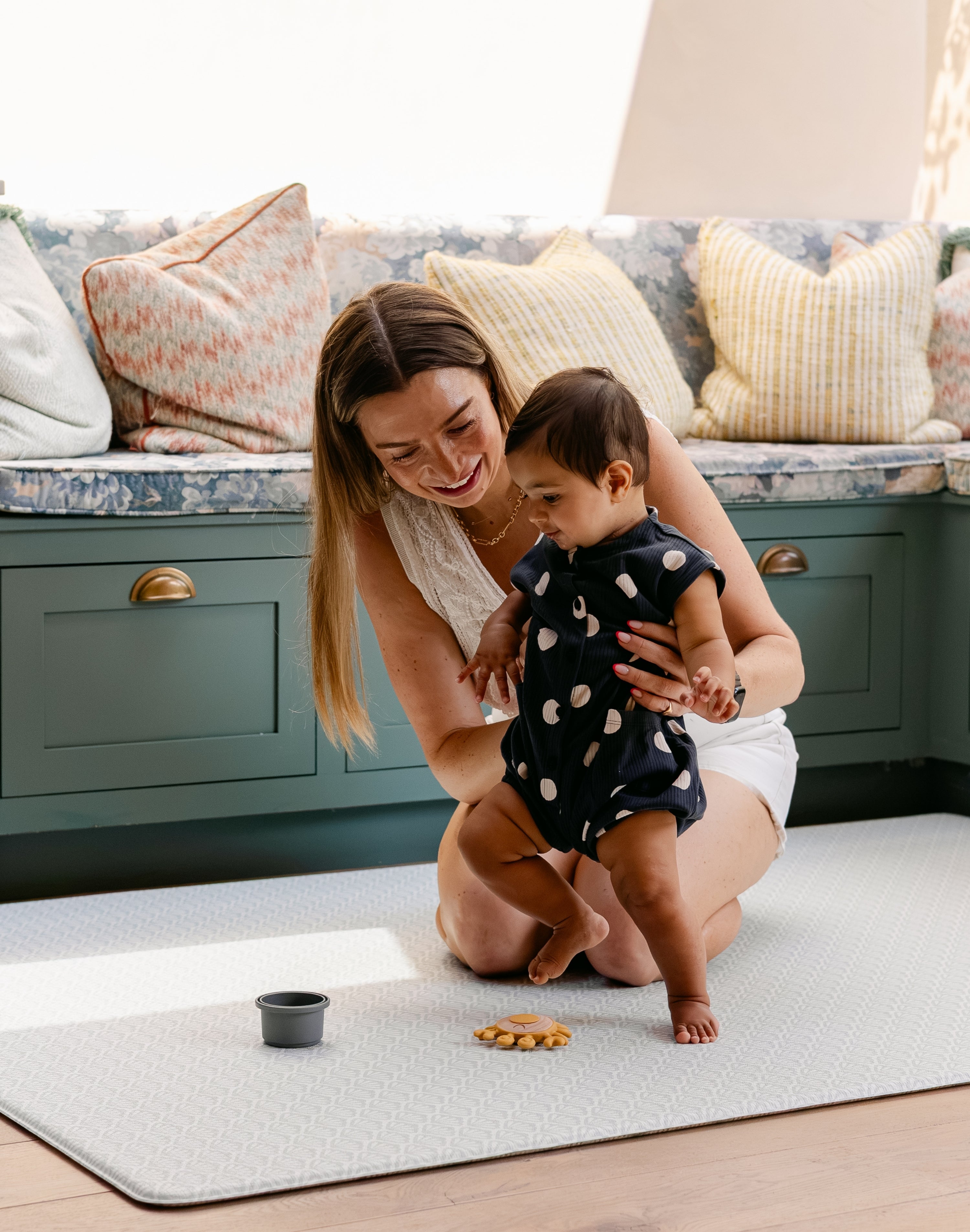 A woman helping a baby take their first steps comfortably and safely on a totter and tumble play mat | SKU: 26 BEACH/GATHER XL, 26 BEACH/GATHER STD, 26 BEACH/GATHER COMP