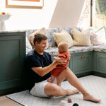A man sat comfortably holding a baby on the gatherer play mat, made from thick safe non toxic memory foam | SKU: 26 BEACH/GATHER XL, 26 BEACH/GATHER STD, 26 BEACH/GATHER COMP