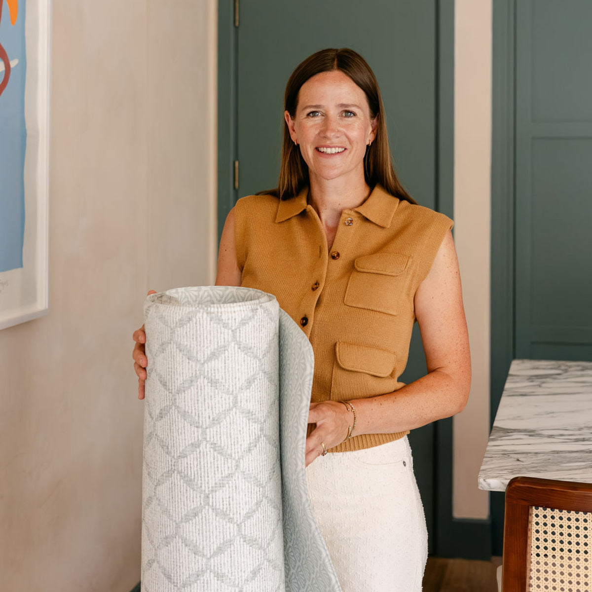 Susie, founder of totter and tumble holding a rolled the gatherer + the beachcomber play mat.
